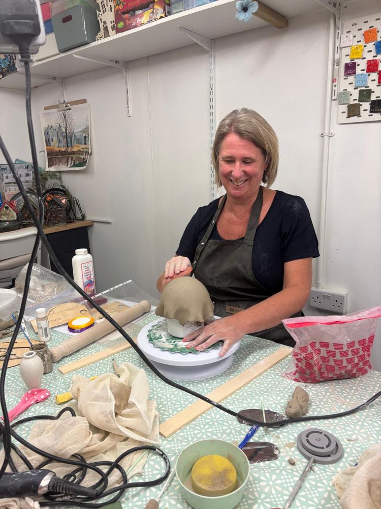 Smiling while shaping a clay piece at the table