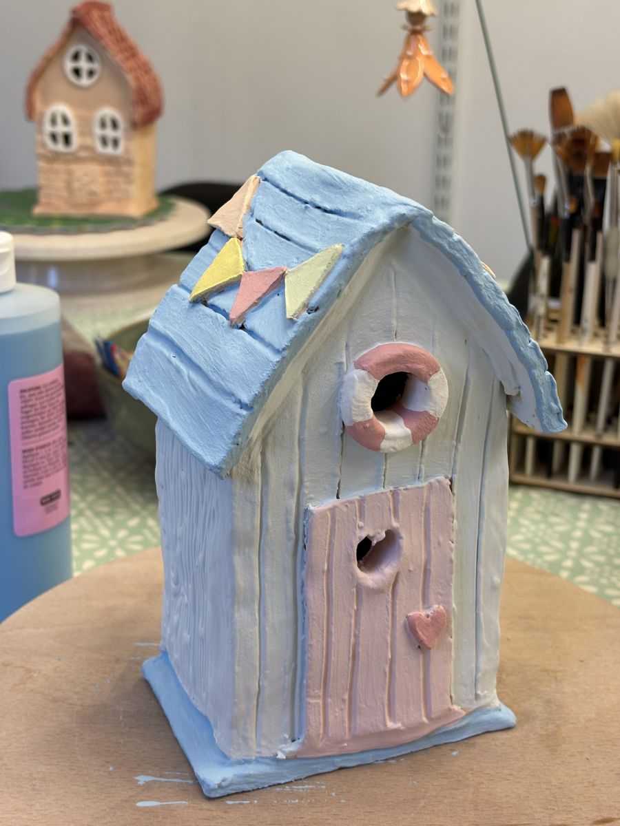 Bisque fired clay beach hut painted blue and pink with a lifebelt and bunting