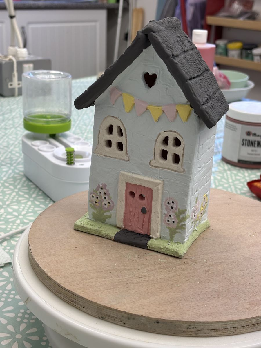 Bisque fired clay house painted with a heart window, bunting and a pink door