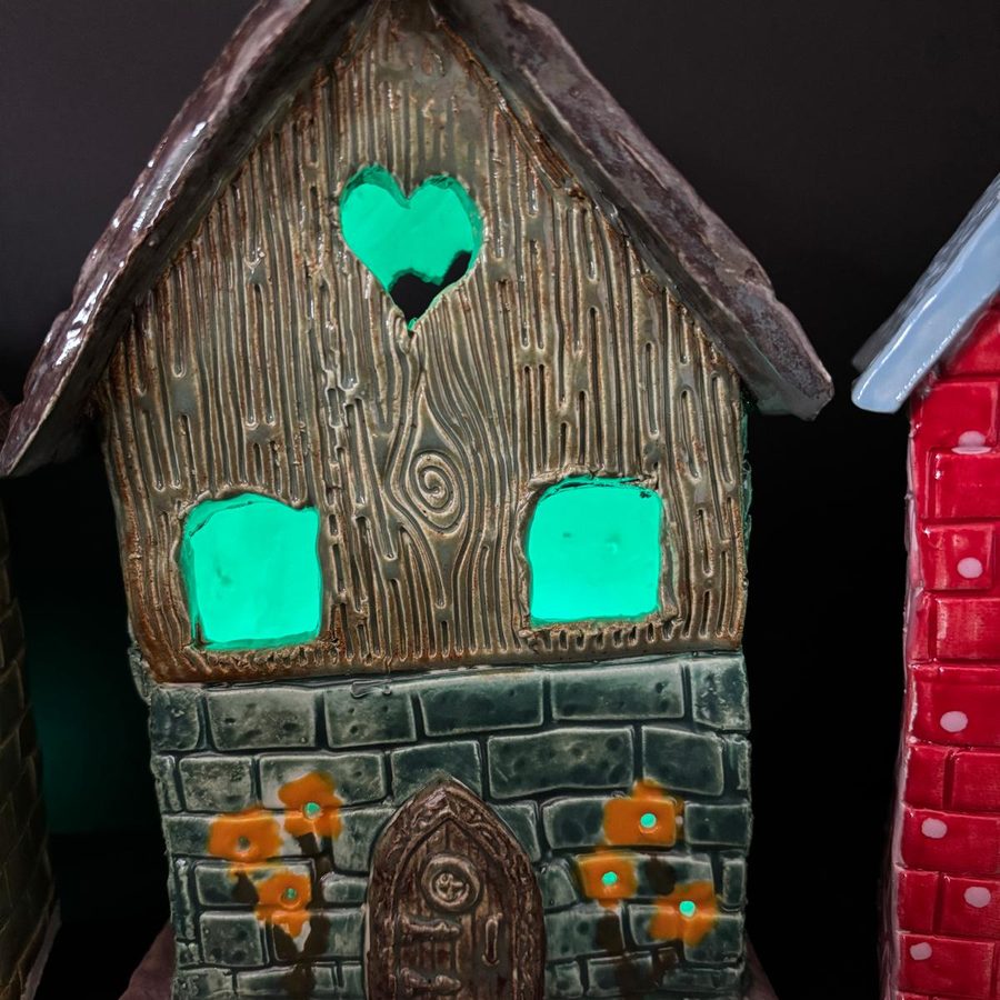 A glazed clay house with a heart window, lit from inside